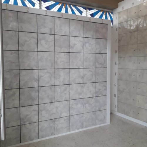 Muro de mosaico gris con numeración, debajo de una ventana con vitral en tonos azules y dorados